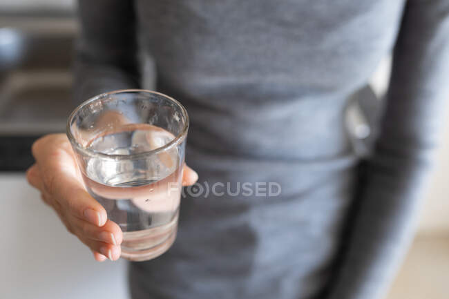 Chiudi la parte centrale della donna che indossa un maglione grigio, con un bicchiere d'acqua in mano. Distanziamento sociale e autoisolamento in quarantena. — Foto stock