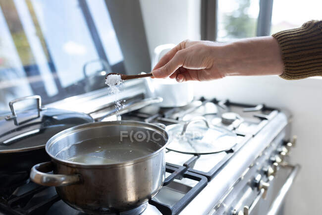 Nahaufnahme einer Frau im Pullover, die Wasser kocht, um Pasta für ihr Mittagessen zu kochen. Soziale Distanzierung und Selbstisolierung in Quarantäne. — Stockfoto