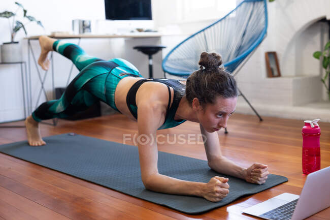 Кавказька жінка проводить час удома, одягаючи спортивну манеру, займаючись спортом, займаючись мате, відвідуючи курси йоги онлайн, використовуючи свій ноутбук. Соціальна дистанція і самоізоляція в карантинному блокуванні.. — стокове фото
