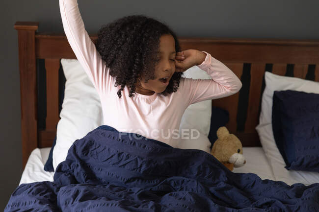 Афроамериканська дівчинка прокидається в батьковій спальні, розтягуючись і позіхаючи, під час соціального дистанціювання вдома під час карантину.. — стокове фото