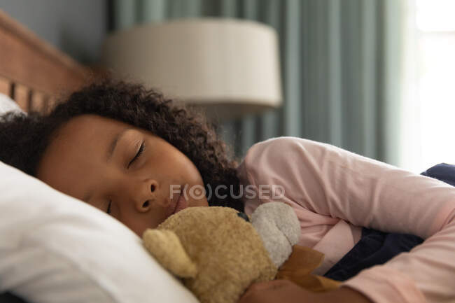 African American girl sleeping in her father bedroom and embracing a teddy bear, during social distancing at home during quarantine lockdown. — Stock Photo