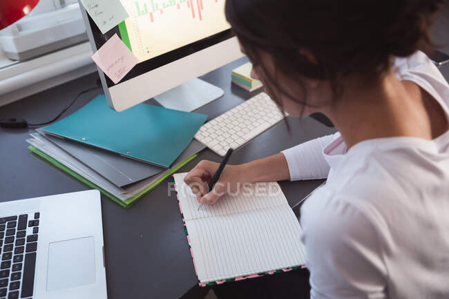 Mixed race woman spending time at home, sitting at desk, taking notes, working from home. Self isolating and social distancing in quarantine lockdown during coronavirus covid 19 epidemic. — Stock Photo