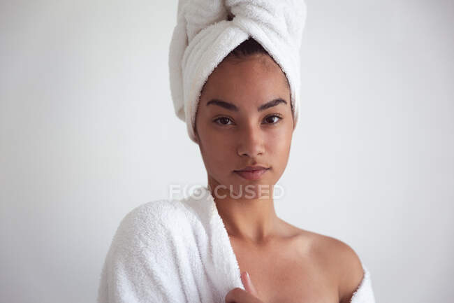 Portrait of mixed race woman spending time at home self isolating and social distancing in quarantine lockdown during coronavirus covid 19 epidemic, wearing bathrobe with towel on her head in bathroom — Stock Photo