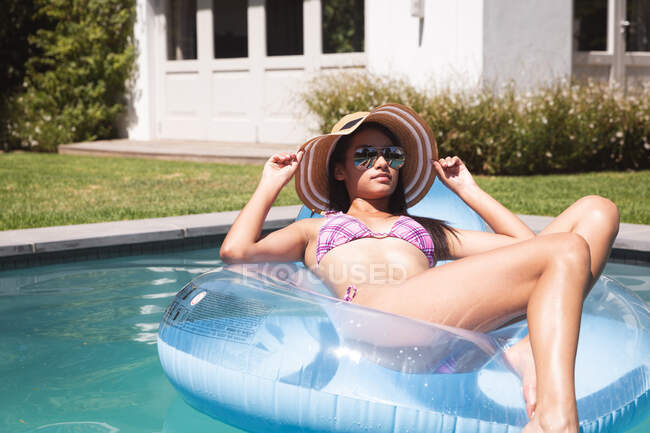Femme de course mixte passant du temps à la maison, assis dans la piscine dans un gonflable et relaxant. Auto-isolement et distanciation sociale en quarantaine pendant l'épidémie de coronavirus covid 19. — Photo de stock