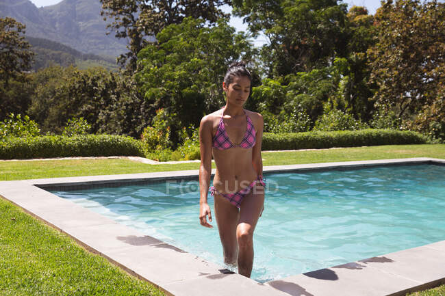 Mixed race woman spending time by swimming pool self isolating and social distancing in quarantine lockdown during coronavirus covid 19 epidemic, walking out of the pool — Stock Photo