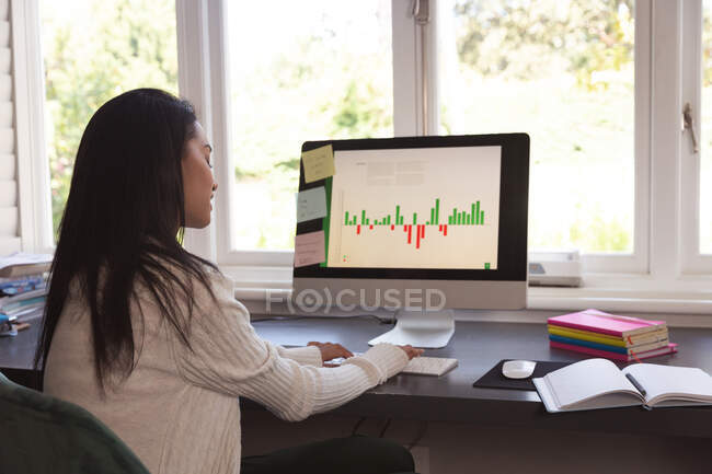 Mixed race woman spending time at home, sitting at desk, using computer, working from home. Self isolating and social distancing in quarantine lockdown during coronavirus covid 19 epidemic. — Stock Photo