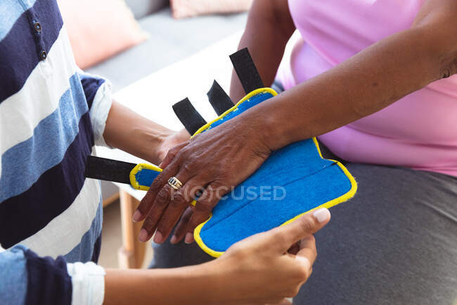 Mid section close up of woman spending time at home, being visited by female nurse, the woman wearing a weight — Stock Photo
