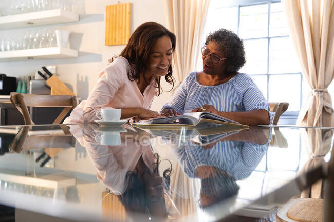 Senior mixed race woman spending time at home with her daughter, social distancing and self isolation in quarantine lockdown, looking at pictures and smiling — Stock Photo