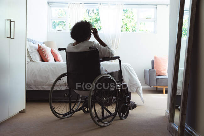 Старшая женщина смешанной расы наслаждается своим временем дома, социальным дистанцированием и самоизоляцией в карантинной изоляции, сидя на инвалидном кресле — стоковое фото