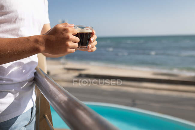 Vue médiane d'un homme debout sur un balcon, tenant une tasse de café. Distance sociale et isolement personnel en quarantaine. — Photo de stock