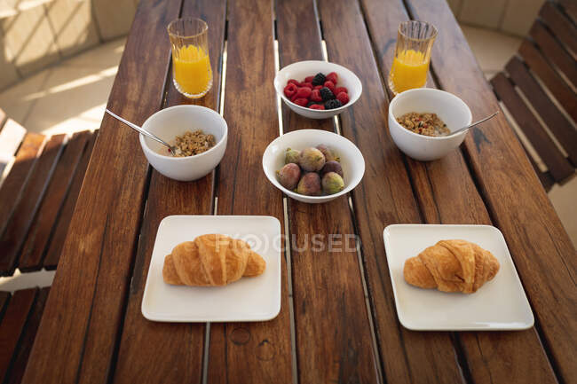 Frühstück auf einem Tisch liegend. Zwei Croissants, zwei Schüsseln Haferflocken, zwei Gläser Saft, eine Schüssel Feigen und eine Schüssel Früchte. — Stockfoto