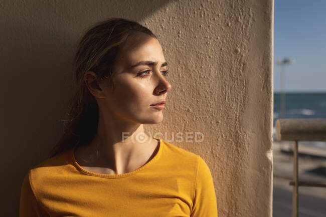 Белая женщина, стоящая на балконе, смотрит в сторону. Социальное дистанцирование и самоизоляция в карантинной изоляции. — стоковое фото