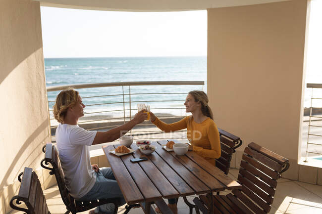 Couple caucasien assis près d'une table, prendre le petit déjeuner, porter un toast. Distance sociale et isolement personnel en quarantaine. — Photo de stock