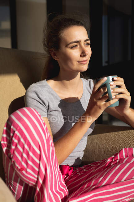 Femme blanche assise sur un balcon, tenant une tasse de café et regardant ailleurs. Distance sociale et isolement personnel en quarantaine. — Photo de stock