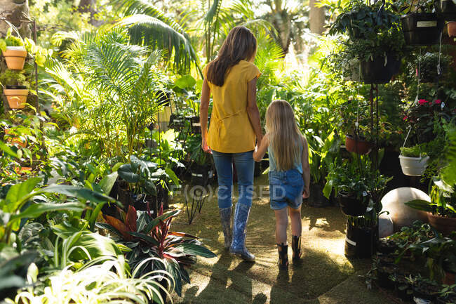 Una donna caucasica e sua figlia si godono il tempo insieme in un giardino in una giornata di sole, indossando galosce, camminando e tenendosi per mano — Foto stock