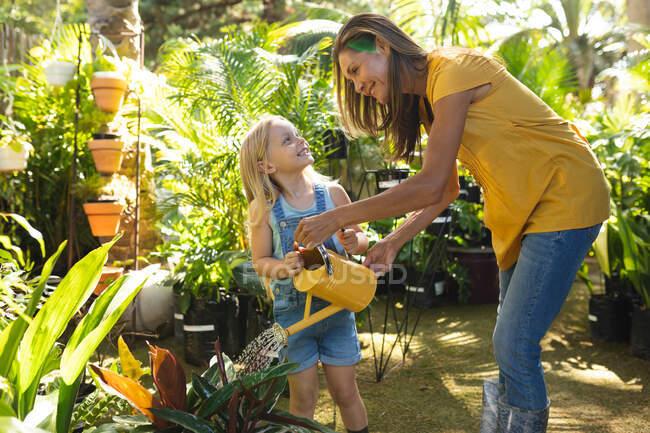 Una donna caucasica e sua figlia godono del tempo insieme in un giardino soleggiato, guardando le piante, innaffiando le piante con annaffiatoio — Foto stock