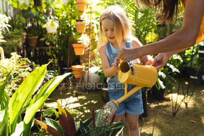 Кавказька жінка з донькою проводять час разом у сонячному саду, спостерігаючи за рослинами, поливаючи рослини водою. — стокове фото