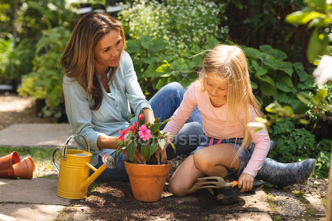 Eine kaukasische Frau und ihre Tochter genießen die gemeinsame Zeit in einem sonnigen Garten und pflanzen einen Sämling in einen Pflanztopf — Stockfoto