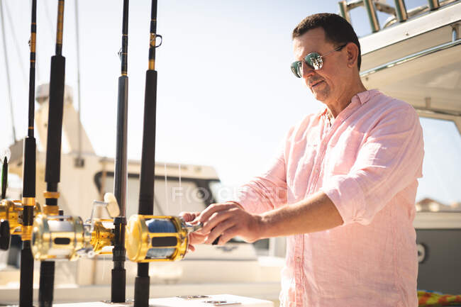 A Caucasian man, wearing a pink shirt and dark sunglasses enjoying his time on a boat, holding a fishing rod — Stock Photo
