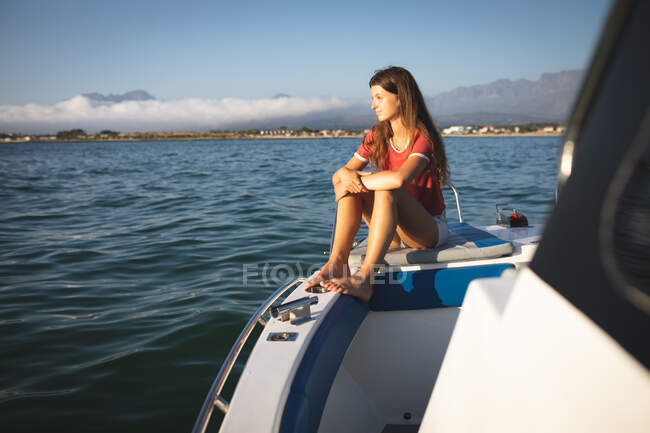 Подросток-кавказка наслаждается отдыхом на солнце у берега, сидит на лодке, расслабляется, смотрит в сторону — стоковое фото