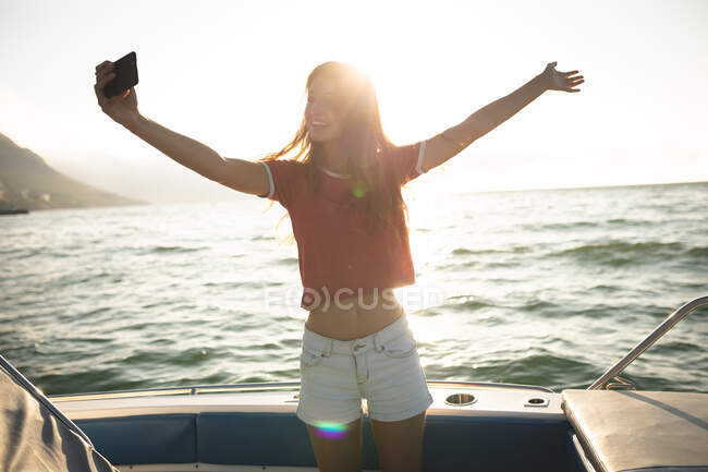 Ein junges kaukasisches Mädchen genießt die Zeit in der Sonne an der Küste, steht auf einem Boot, macht ein Selfie und lächelt — Stockfoto