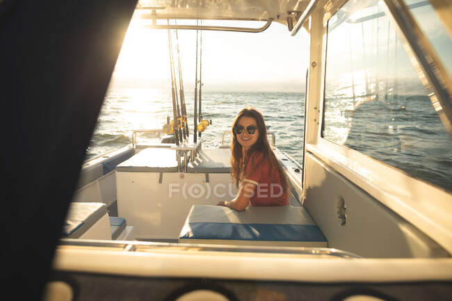Ritratto di una ragazza caucasica adolescente che si gode il suo tempo in vacanza al sole vicino alla costa, seduta su una barca, guardando la macchina fotografica e sorridendo — Foto stock