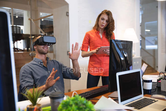 Caucasian female and male business creatives working in a casual modern office, a man using a VR headset and a woman using a tablet — Stock Photo