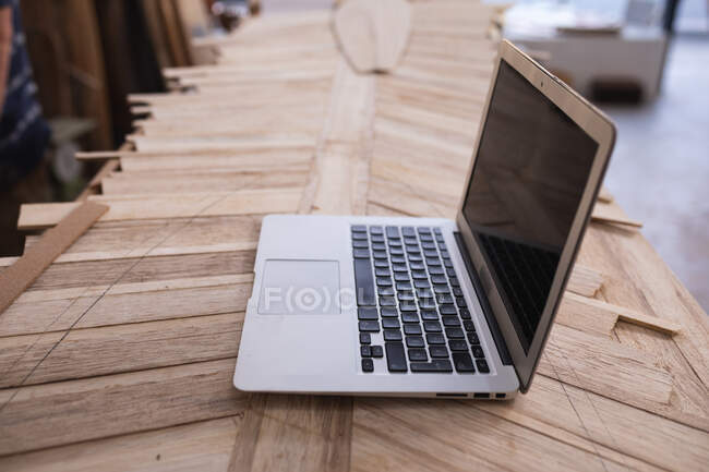 Vista de perto de um computador portátil colocado em uma prancha de surf em construção em um estúdio de fabricantes de pranchas de surf . — Fotografia de Stock