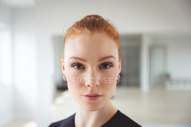 Portrait of a Caucasian attractive female ballet dancer with red hair preparing for a ballet class in a bright studio, staring to camera with a slight smile — Stock Photo