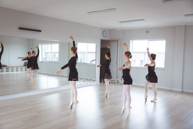 Група кавказьких танцюристок в чорному вбранні під час класу балету в яскравій студії танцюють перед дзеркалом.. — стокове фото
