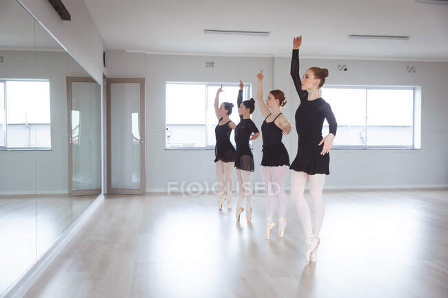 Група кавказьких танцюристок у чорних костюмах, що танцюють під час класу балету у яскравій студії, танцюють перед дзеркалом.. — стокове фото