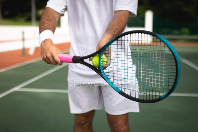 Nella parte centrale dell'uomo che indossa i bianchi del tennis trascorre del tempo su un campo a giocare a tennis in una giornata di sole, con una racchetta da tennis e una palla — Foto stock