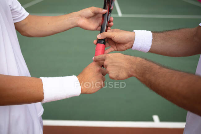 Середня секція крупним планом чоловіки, які носять тенісні білі, проводять час на дворі разом, граючи в теніс в сонячний день, тримаючи тенісну ракетку — стокове фото