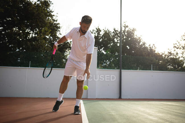 Un uomo di razza mista che indossa i bianchi del tennis trascorre del tempo su un campo a giocare a tennis in una giornata di sole, preparandosi a colpire una palla — Foto stock
