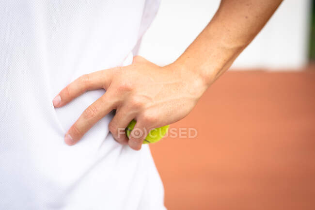 Primo piano di una mano di uomo che indossa i bianchi del tennis che trascorre del tempo su un campo a giocare a tennis in una giornata di sole, tenendo una palla da tennis — Foto stock