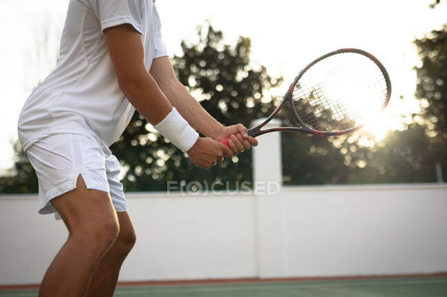 In der Mitte ein Mann in weißen Tennisanzügen, der an einem sonnigen Tag mit einem Tennisschläger auf einem Tennisplatz spielt — Stockfoto