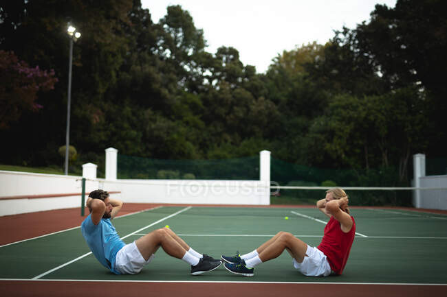 Белый и смешанная раса мужчин, проводящих время на корте вместе, играющих в теннис в солнечный день, упражняющихся — стоковое фото