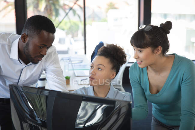 Groupe multiethnique de collègues masculins et féminins travaillant dans un bureau moderne, assis à un bureau, utilisant un ordinateur et discutant de leur travail — Photo de stock
