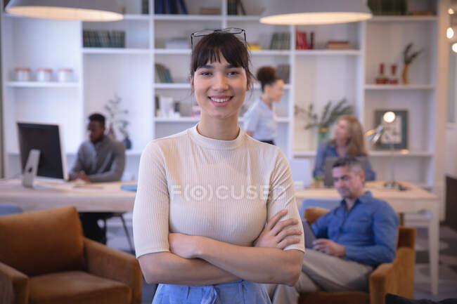 Ritratto di una felice donna d'affari asiatica che lavora in un ufficio moderno, guarda la macchina fotografica e sorride, con i suoi colleghi che lavorano sullo sfondo — Foto stock