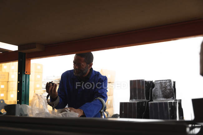 An African American male worker in a storage warehouse at a factory making wheelchairs, standing and inspecting parts on shelves — Stock Photo