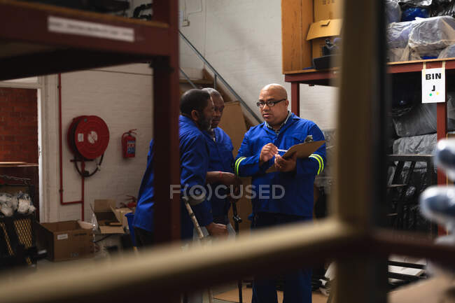 Three of Caucasian and African American male workers in a storage warehouse at a factory making wheelchairs, standing and talking, two of them are disabled and using crutches — Stock Photo