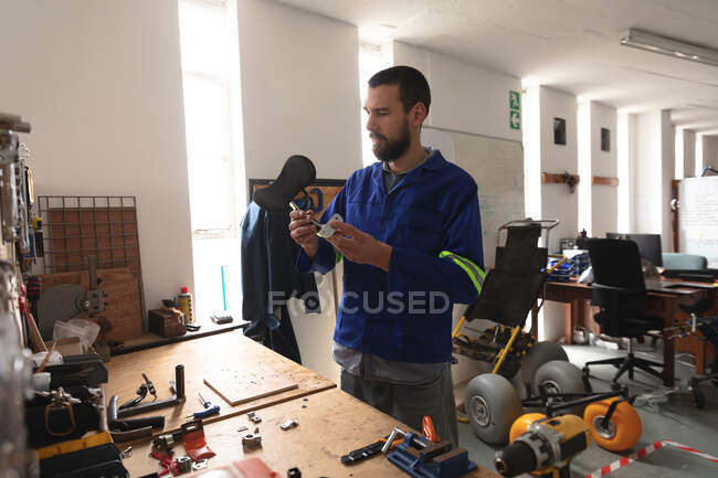 A Caucasian male worker in a workshop at a factory making wheelchairs, standing at a workbench and inspecting parts, wearing a workwear — Stock Photo
