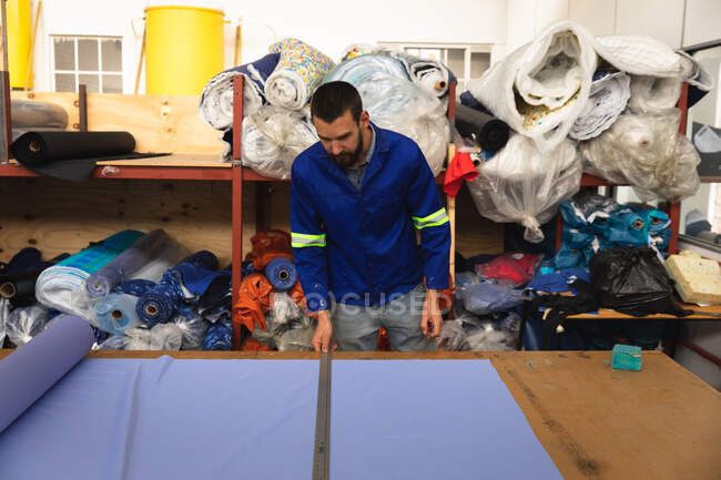 Un ouvrier caucasien dans un atelier d'une usine fabriquant des fauteuils roulants, debout sur un établi, utilisant une règle en métal et un matériau de marquage — Photo de stock