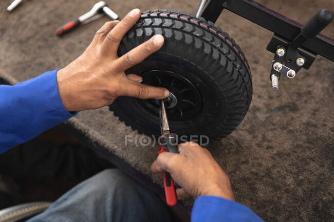 Close up of a male worker in a workshop at a factory making wheelchairs, sitting at a workbench assembling parts of a product, sitting in wheelchair — Stock Photo