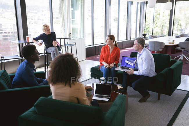 Multi-ethnic group of male and female colleagues working in a modern office, meeting in a lounge area discussing business and their work — Stock Photo