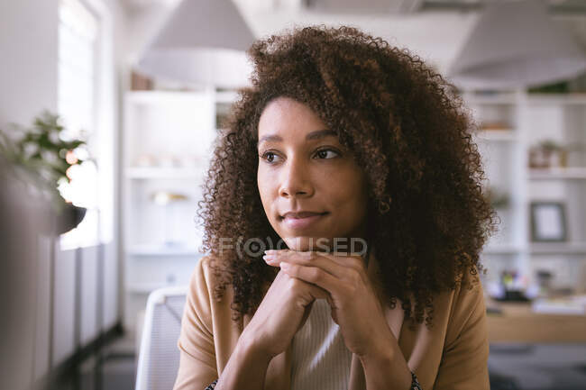 Gros plan d'une femme d'affaires métisse travaillant dans un bureau moderne, assise à un bureau, regardant ailleurs et pensant — Photo de stock