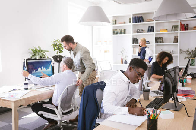 Groupe multi-ethnique de collègues d'affaires masculins et féminins travaillant dans un bureau moderne, assis à un bureau, utilisant des ordinateurs, discutant de leur travail — Photo de stock