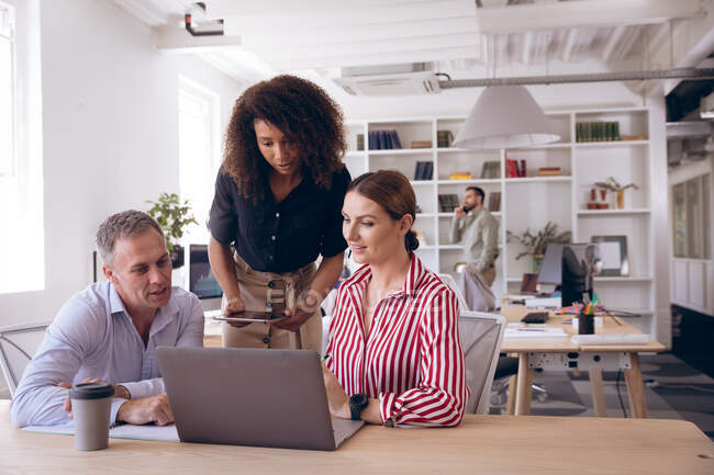 Multiethnische Gruppe männlicher und weiblicher Geschäftskollegen, die in einem modernen Büro arbeiten, am Schreibtisch sitzen, Laptop und Tablet benutzen und über ihre Arbeit diskutieren — Stockfoto
