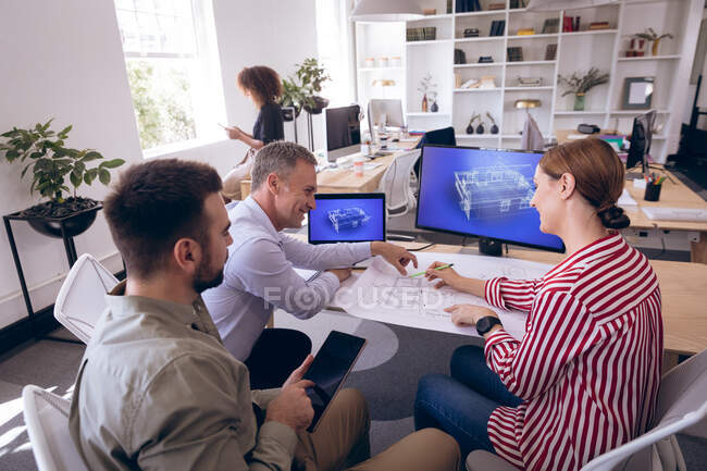 Un groupe caucasien de collègues d'affaires masculins et féminins travaillant dans un bureau moderne, assis à un bureau, regardant des plans, utilisant une tablette, discutant de leur travail ensemble — Photo de stock