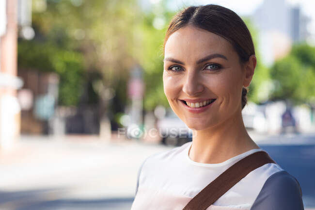 Porträt einer kaukasischen Geschäftsfrau, die an einem sonnigen Tag unterwegs ist, modische Kleidung trägt, in die Kamera blickt und lächelt — Stockfoto